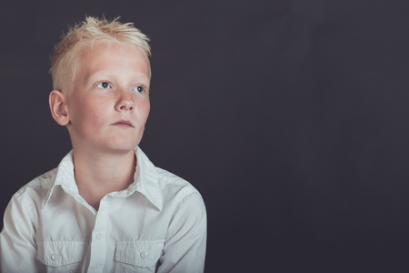 Pensive young boy in spiked blond hair looking upward over black background with copy spaceの写真素材