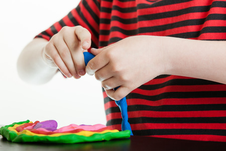 Hands of a young boy playing with bright colorful pieces of plastic putty molding it with his hands into tubes to incorporate into his designの写真素材