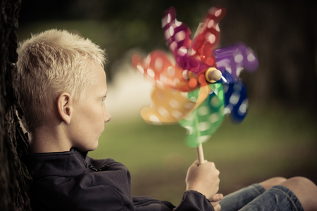 Close up view of blond child holding windmill colored green, blue and yellow as it spinsの写真素材