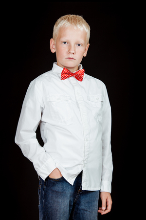 Serious boy stands with one hand in jean pocket while wearing a white shirt and red polkadot bow tieの写真素材