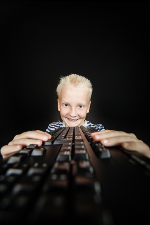 Smiling blond youth holds keyboard in both hands against a black backgroundの写真素材