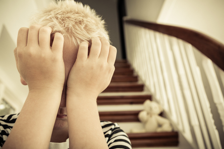 Close up of child with hands against his face sits in stairwell near discarded teddy bearの写真素材