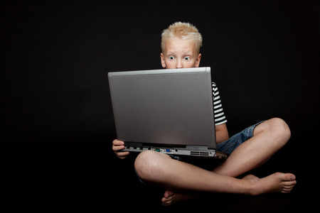 Boy sitting cross legged wearing stripped shirt is surprised as he works on laptop computerの写真素材