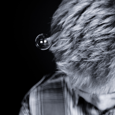 Black and white top down view on bubble attached to hair of unidentifiable boy looking downward over black backgroundの写真素材