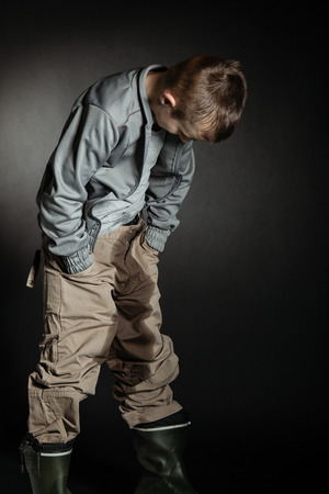 Lonely boy stares at his oversized clothes while holding both hands in the pant pocketsの写真素材