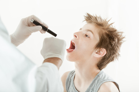 Doctor in gloves checking up boy throat with flashlight, on white backgroundの写真素材