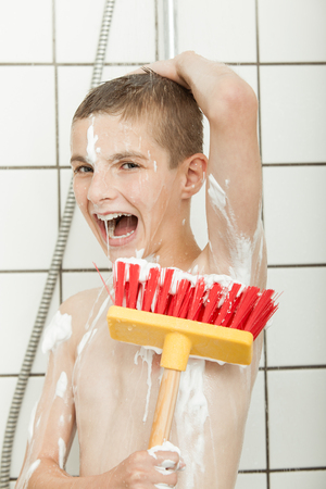 Little boy screaming or laughing lathering his armpit using big red broom brush in showerの写真素材