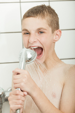 Young boy clowning in the shower by trying to bite shower headset with water flowing to his wide open mouthの写真素材