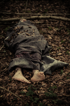 Murder victim lying covered in sheets with bare feet protruding on leafy groundの写真素材