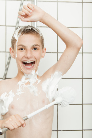 Young boy laughing as he lathers himself with soap suds in shower using a wooden toilet brush to clean under his armpitsの写真素材
