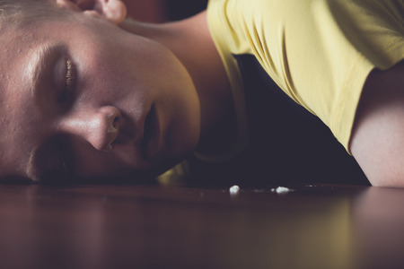 Young teenage drug addict snorting cocaine passed out on the table with remnants of the powder coating his nostrils, close up viewの写真素材