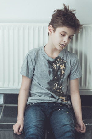 Young boy slumped against a radiator with vomit spewed down his t-shirt front in a conceptual image of drug abuse or healthcare and medicineの写真素材