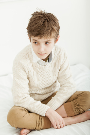 Thoughtful young boy sitting cross legged on his bed staring to the side with a pensive serious expressionの写真素材
