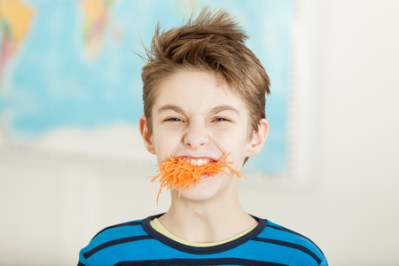 Young boy with a mouthful of grated carrot screwing up his face in aversion and disgust in a healthy diet conceptの写真素材
