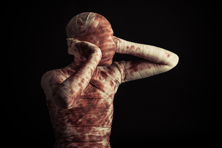 Halloween horror with a bloodstained bandaged mummy or accident victim standing holding its ears on a black background with copy spaceの写真素材