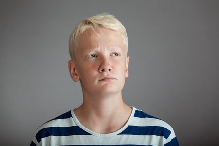 Front view on blond boy with concerned expression in blue and white striped shirt over gray backgroundの写真素材
