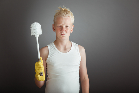 Single blond angry child in white shirt holding toilet scrubber for concept about children hating choresの写真素材