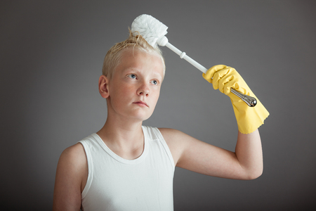 Single child in white undershirt holding toilet scrubber above his head as he brushes his hair with itの写真素材