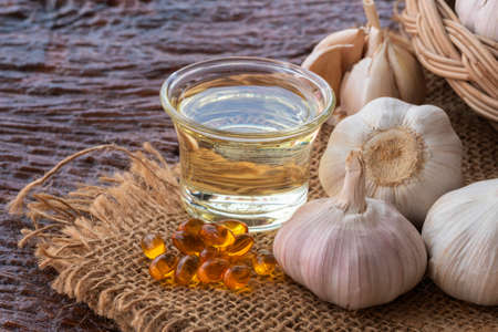 Garlic bulb and garlic oil on sackcloth on rough wooden background.の写真素材