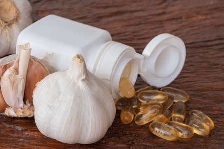 Garlic bulbs ( Allium sativum L.), capsules of garlic oil, and white bottle on  brown wooden background.の写真素材