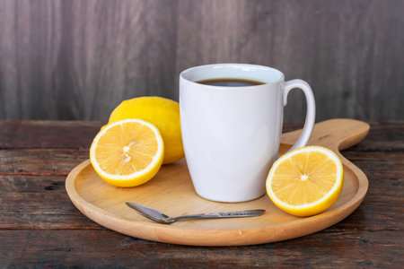 Black coffee lemon in white cup, coffee beans, lemon fruit, and lemon slices on wooden saucer and on vintage brown wooden background.の写真素材