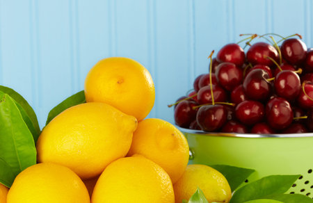 Lemons With Green Leaves and Ripe Red Cherries In Green Colander ~ Blue Backgroundの写真素材