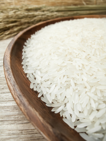 Close up white rice on the wooden plate and background is rice plant , uncooked raw cerealsの写真素材