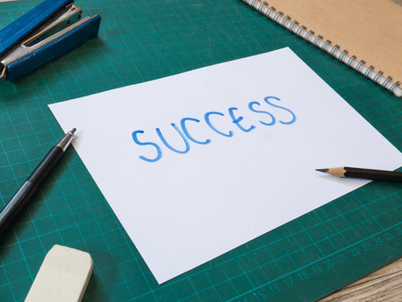 Stationery and hand writing success text paper on cutting mat.And all on wooden backgroundの写真素材