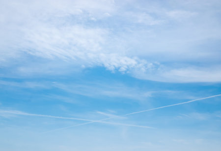 softly clouds in the blue sky background with airplane exhaust streams showing crossind lines.