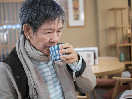 Senior Asian woman drinking  cup of hot tea in the restaurantの写真素材