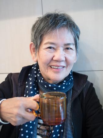 Senior Asian woman holding cup of water and relaxing in the restaurantの写真素材