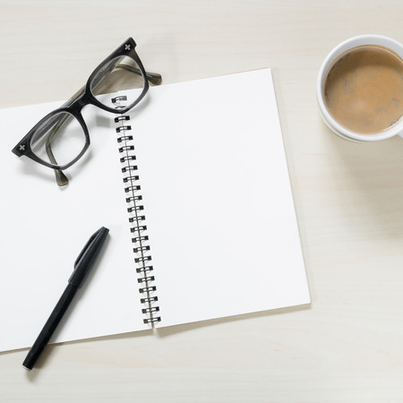 Work place - Blank notebook with vintage eyeglasses, pen and cup of hot coffee on wooden table ( Space and composition for text )の写真素材