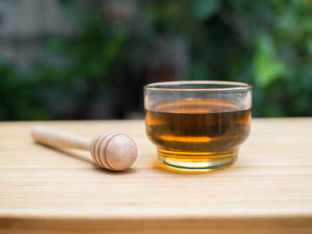 Glass cup of honey and honey dipper on wooden backgroundの写真素材