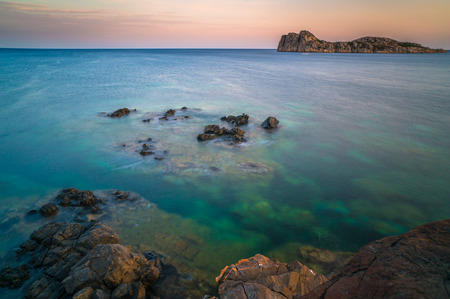 surreal sunset at a rocky coast with island in the background. Turqouise clear sea. Sardinia, Italy.の写真素材