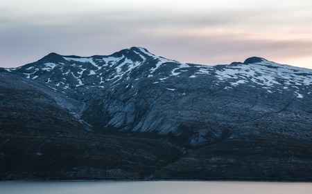 Midnight sun glowing behind the mountain at a norwegian fjordの写真素材