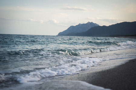 detail shot of wave splashing to the beach, mountains in the background.