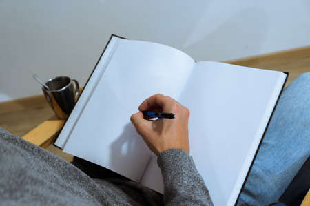 young male student taking notes. Hand drawing on a blank book on an armchair. over the shoulder view.の写真素材