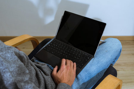 Young man holding laptop in lap, working on it, photographed from behind. white screen.