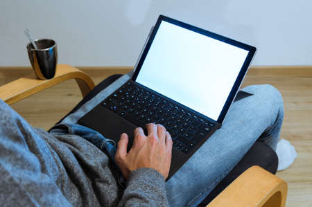 Young man holding laptop in lap, working on it, photographed from behind. black screen with coffeeの写真素材