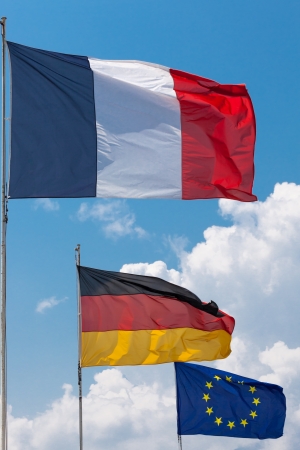 French, German and European Union Flags flying in the wind under a sun filled sky with towering cumulus clouds in the backgroundの写真素材