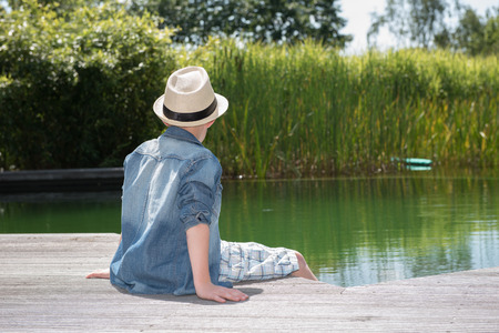 little boy sitting at the pool and looking into the waterの写真素材
