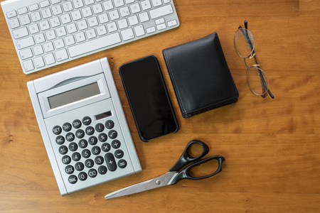 wooden desk with keyboard, smartphone, calculator and scissorsの写真素材
