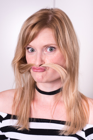 beautiful blonde woman is making a mustache with her hairの写真素材