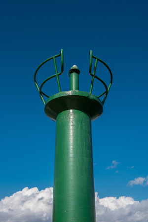 Green position light at the harbor entrance against a blue skyの写真素材