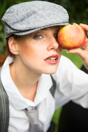 red-haired woman with cap in the garden holds apple before the eyeの写真素材