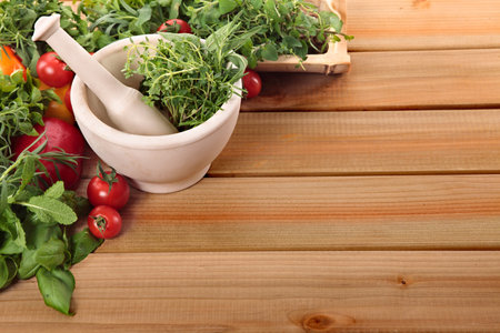 Fresh herbs with a mortar and pestle and vegetables on a wooden worktop. Space for copy.の写真素材