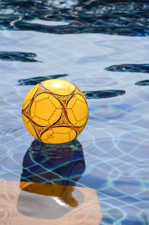 Multicolored beach ball floating on a sparkling blue swimming poolの写真素材