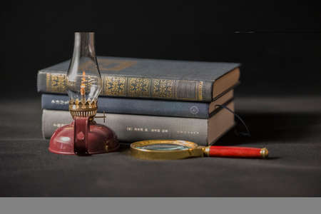 An old kerosene lamp, magnifying glass and booksの写真素材