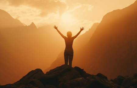 The silhouette of a tourist standing with his arms outstretched the golden glow of the morning sun on the mountaintop. Standing up to achieve success.の素材