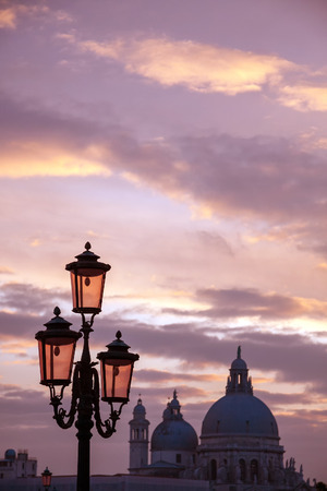 Italy Venice island city at sunset view over the gondola poles to Santa Maria della Salute cathedral over canal illuminated Murano glass lampsの写真素材